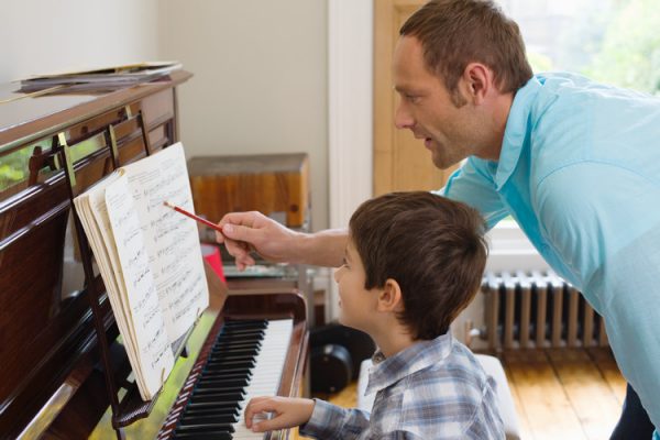 father teaching son how to play the piano